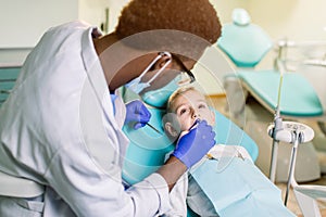 Teeth checkup at dentist`s office. African-American dentist examining boy`s teeth in the dentists chair