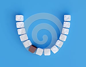 Teeth from sugar cubes on blue background, some brown sugar teeth, concept for sweet tooth, caries