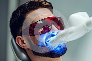 Teeth whitening. Man having teeth whitened by dental UV laser whitening device. Teeth whitening machine,eyes protected with photo