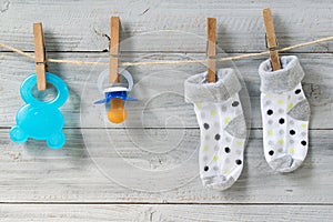 Teether, baby pacifier and socks hanging on clothesline on wooden background