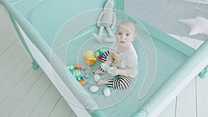 Teething infant biting toy eggs in playpen at home