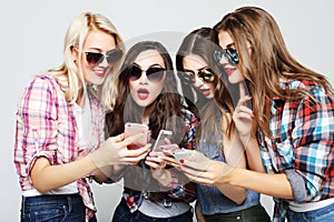 Tehnology, emotion and people concept: four happy women friends sharing social media in a smart phone