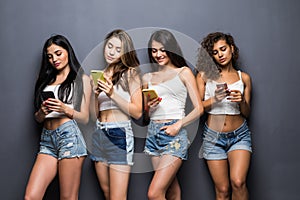 Tehnology, emotion and people concept: four happy women friends sharing social media in a smart phone, over gray background