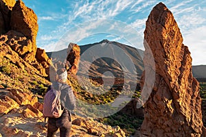 Teide- Woman with backpack hiking with scenic golden hour sunrise morning view on unique rock formation Roque Cinchado, Tenerife.