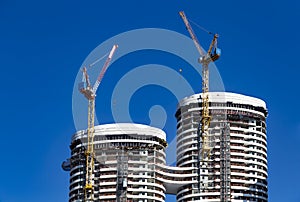 Two building crane attached to the construction of a modern high-rise building at the