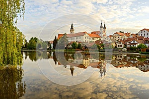 Telc with historical buildings, church and a tower. Buildings in water reflection
