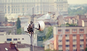 Telecommunication microwave antenna dish on a building rooftop with the city in background