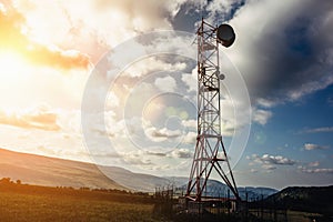 Telecommunication tower with dish and mobile antenna on mountains at sunset sky background