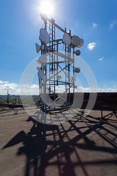 Telecommunication tower with microwave, radio antennas and satellite dishes with shadows on the roof