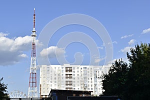 A telecommunications antenna in the city and a Ferris wheel with a big house and a blue sky