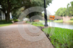 Telecommunications cable stake flag buried underground utility beside a footpath and river