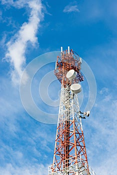 Telecommunications tower with many satellite dish on blue sky cloud background.