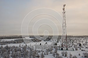 Telecommunications tower and satellite dish telecom network on evening sky with sundown and winter north forest