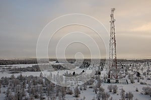 Telecommunications tower and satellite dish telecom network on evening sky with sundown and winter north forest