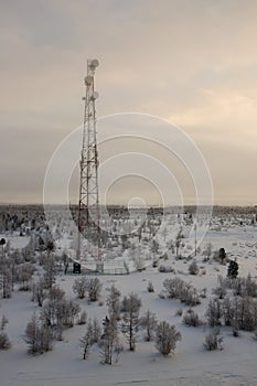 Telecommunications tower and satellite dish telecom network on evening sky with sundown and winter north forest