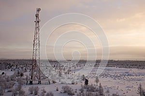 Telecommunications tower and satellite dish telecom network on evening sky with sundown and winter north forest