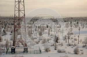 Telecommunications tower and satellite dish telecom network on evening sky with sundown and winter north forest