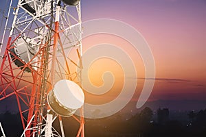 Telecommunications tower and satellite dish telecom network with silhouette of countryside area in sunrise