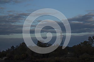 The telecommunications tower stands on a hill under a cloudy sky. Autumn landscape.