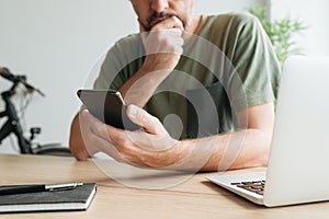 Telecommuter reading text message on mobile smart phone in home office photo