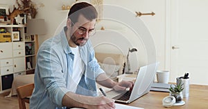 Telecommuting employee sit at desk working on laptop and papers