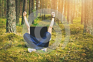 Telecommuting - man with laptop laying in the moss in the forest with hands raised