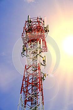 Telecoms tower with transmitter antenna on the bright blue sky and sun flare background