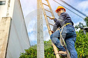 A telecoms worker is shown working from a utility pole ladder while wearing high visibility personal safety clothing, PPE, and a