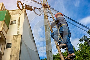 A telecoms worker is shown working from a utility pole ladder while wearing high visibility personal safety clothing, PPE, and a