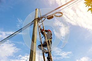 A telecoms worker is shown working from a utility pole ladder while wearing high visibility personal safety clothing, PPE, and a