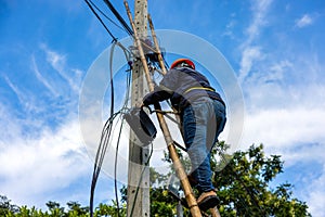 A telecoms worker is shown working from a utility pole ladder while wearing high visibility personal safety clothing, PPE, and a