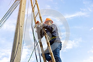 A telecoms worker is shown working from a utility pole ladder while wearing high visibility personal safety clothing, PPE, and a