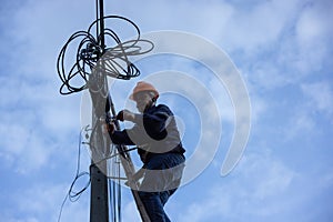 A telecoms worker is shown working from a utility pole ladder while wearing high visibility personal safety clothing, PPE, and a