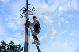 A telecoms worker is shown working from a utility pole ladder while wearing high visibility personal safety clothing, PPE, and a