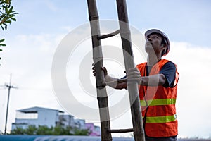 A telecoms worker is shown working from a utility pole ladder while wearing high visibility personal safety clothing, PPE, and a