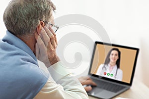 Telehealth concept. Senior man having online video call with doctor on laptop computer at home