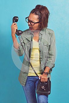 Telephone, angry and shouting with woman, stress and frustrated on blue studio background. Person, furious and girl with