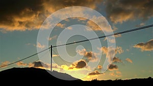 Telephone line against the blue and orange sky at sunset with moving colorful clouds.