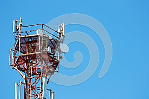 A telephone metal tower of red and white radio communication hung with equipment and satellite dishes against the blue sky. Modern