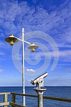 Telescope with coin slot and lantern on the pier in Bansin on the island of Usedom in Germany. Sea and sky are dark blue and radia