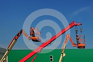 Telescopic crane and two aerial platforms of cherry pickers in a construction site photo