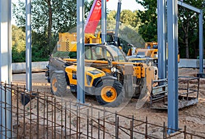 Telescopic handler against the background of a mobile crane at a construction site in the evening after work
