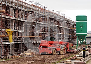 Telescopic handler between a building under construction covered with scaffolding and a concrete batching silo