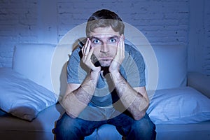 Television addict man at home lying on couch watching tv holding remote control