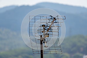 Television antenna from a roof in a rural village house with the mountains out of focus in the background.