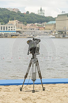 Television camera on the river beach. Lonely camcorder on a tripod. Vertical photo