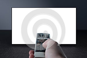 Television on gray wall and remote control in hand. Watching online TV. TV 8K flat screen oled with White blank screen. TV mockup