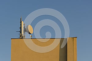 A television telecommunications antenna on clear blue day sky mounted on the roof of yellow square building as a background.