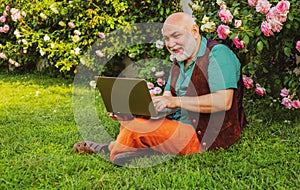 Telework concept. Senior man in garden with laptop. Old gardener online social network games.