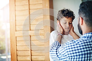 Tell me how I can help to cheer you up...a sad little boy being comforted by his father at home.